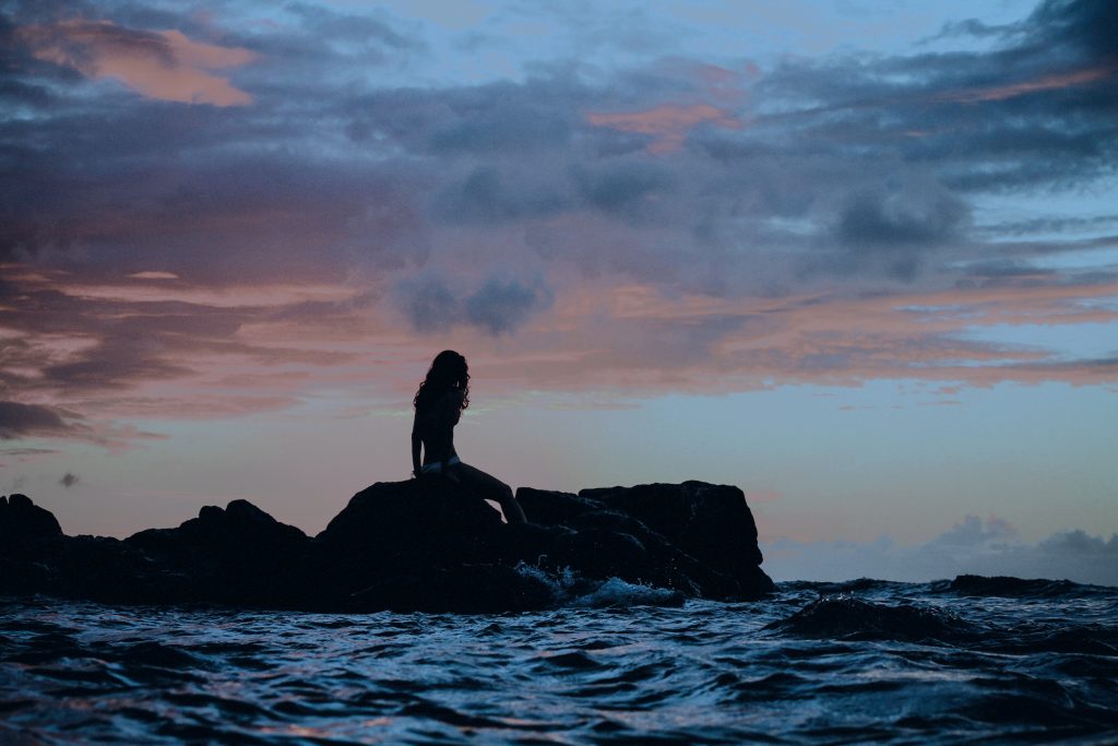 Woman sitting on a rock by the shore.