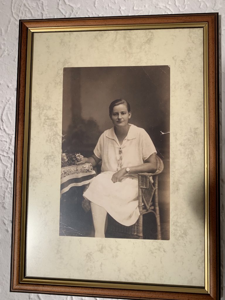 Black and white photograph of a young woman sitting. She is wearing a white dress and is slightly smiling.